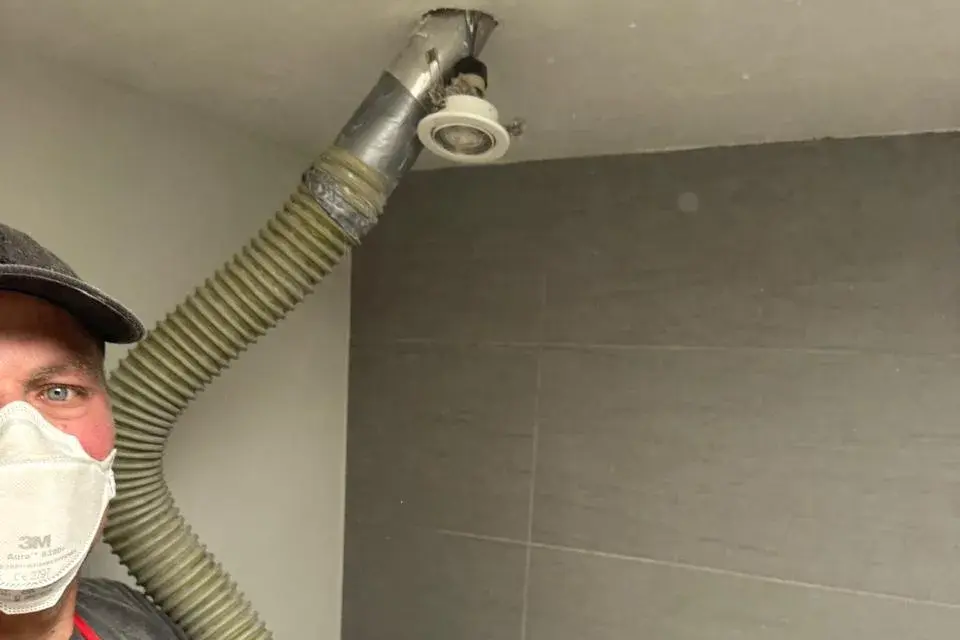 Foto van ons werk: monteur met stofmasker houdt de inblaasslang in een gat in het plafond