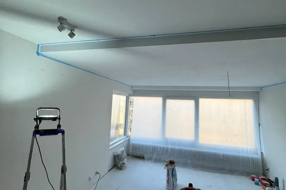 Foto van ons werk: lege kamer met afgedekte vloer en afgeplakte randen, klaar voor het werk